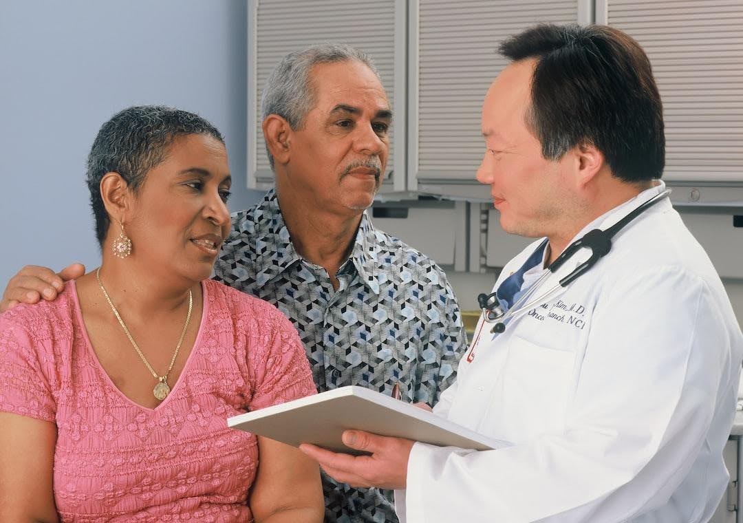 A male doctor in a white lab coat talking to an older couple in a clinical setting, illustrating a consultation about pelvic health
